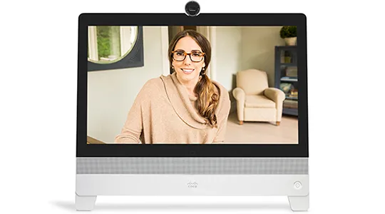 Monitor displays a smiling woman wearing glasses, with an armchair and shelving visible behind her.