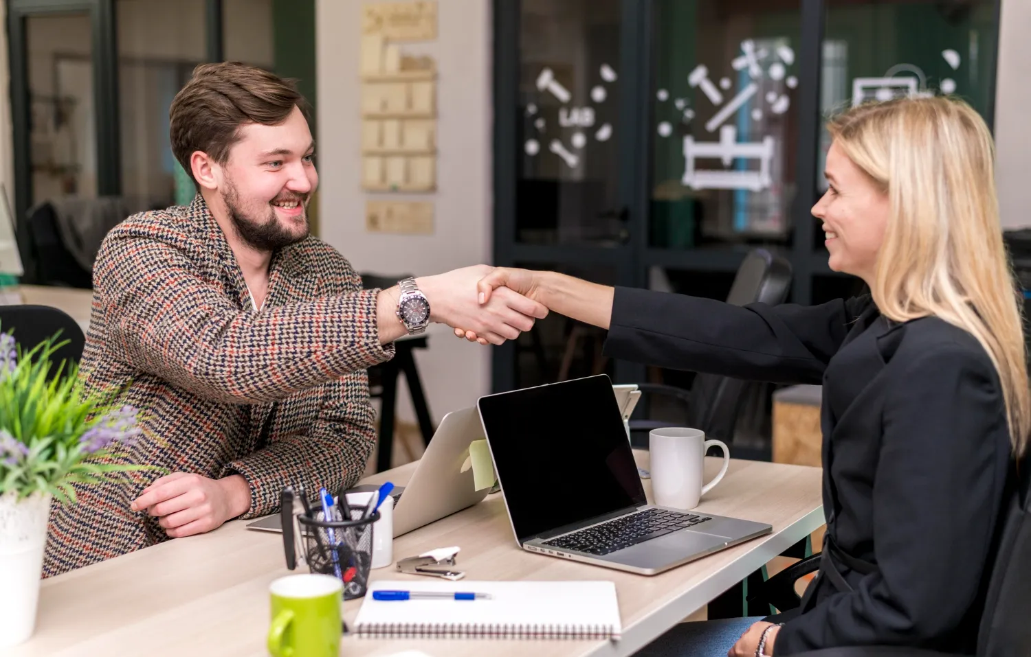 Professional business handshake in modern office with laptop setup.