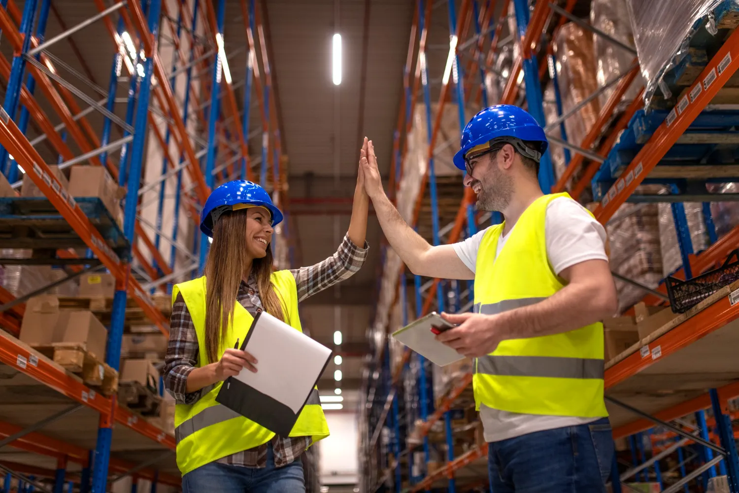 Warehouse team in safety gear celebrating with high-five, collaboration