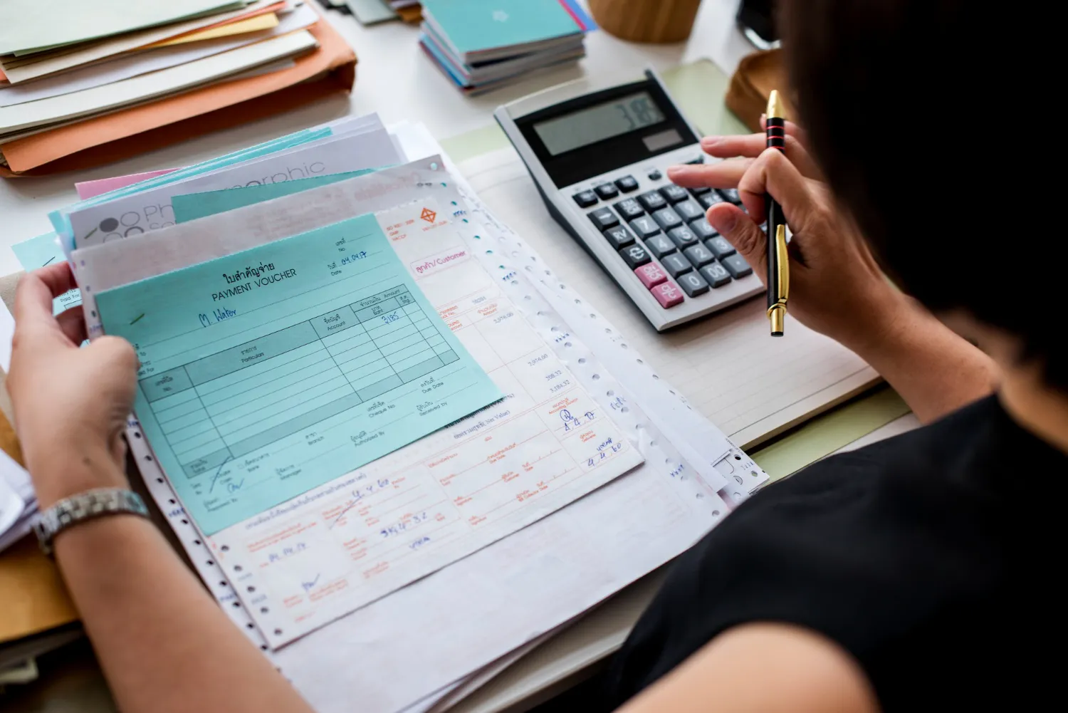 Accountant calculating payment vouchers with pen on tidy desk.