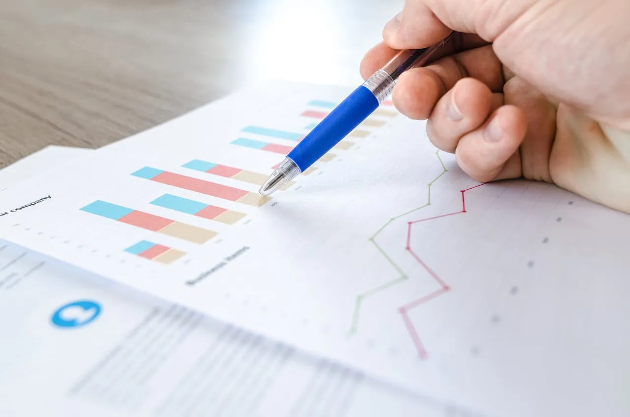Hand holding pen analyzing printed bar and line charts during strategy meeting.