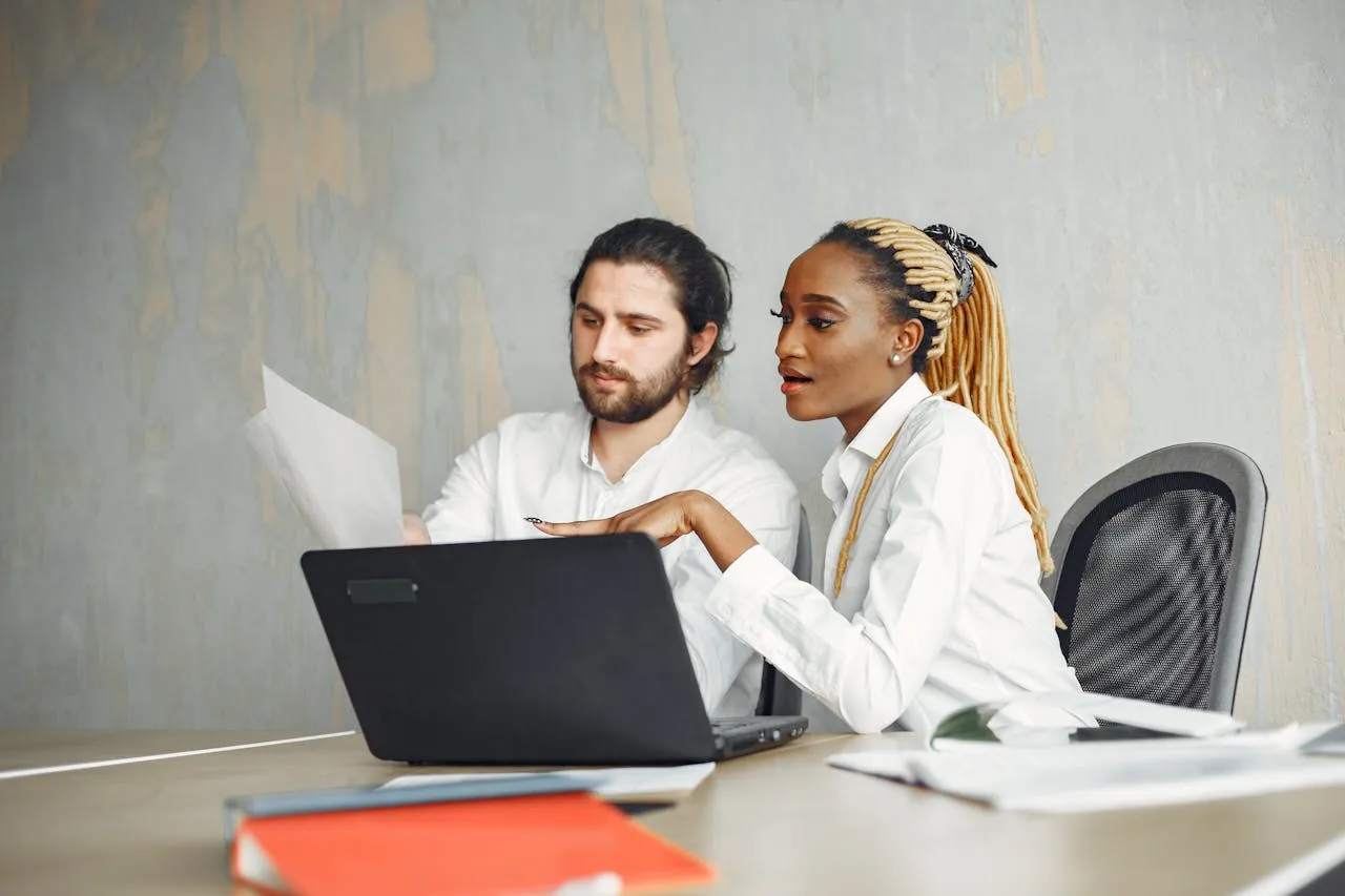 A diverse business team collaborates on a laptop and documents at a modern office desk.