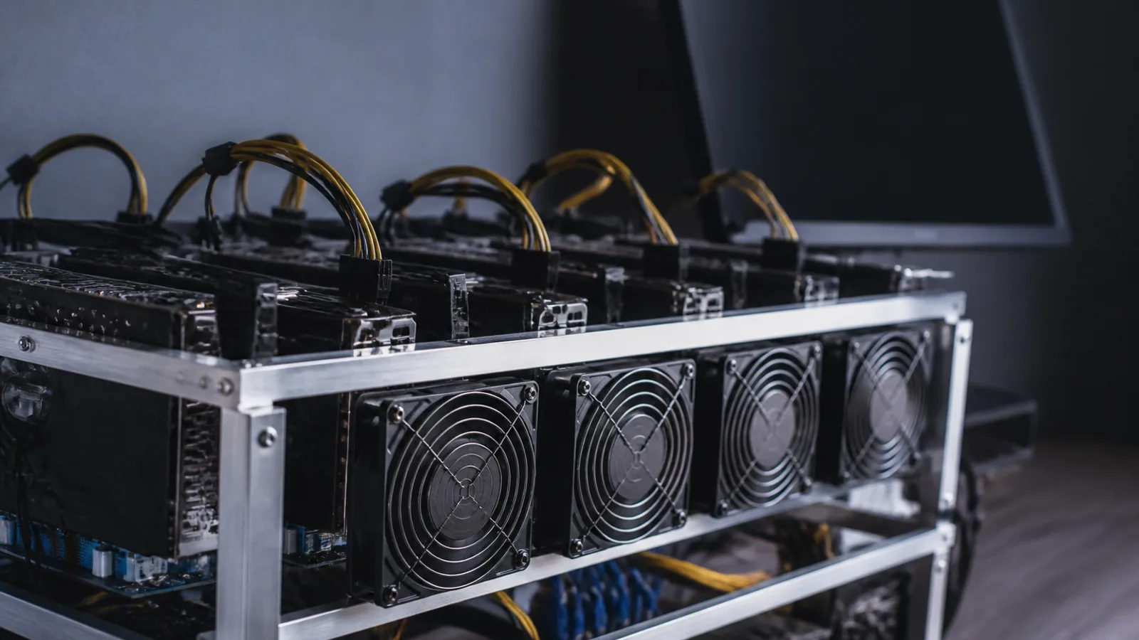 Graphics cards, cooling fans, power cables, and metal mining frames fill a dim utility room.